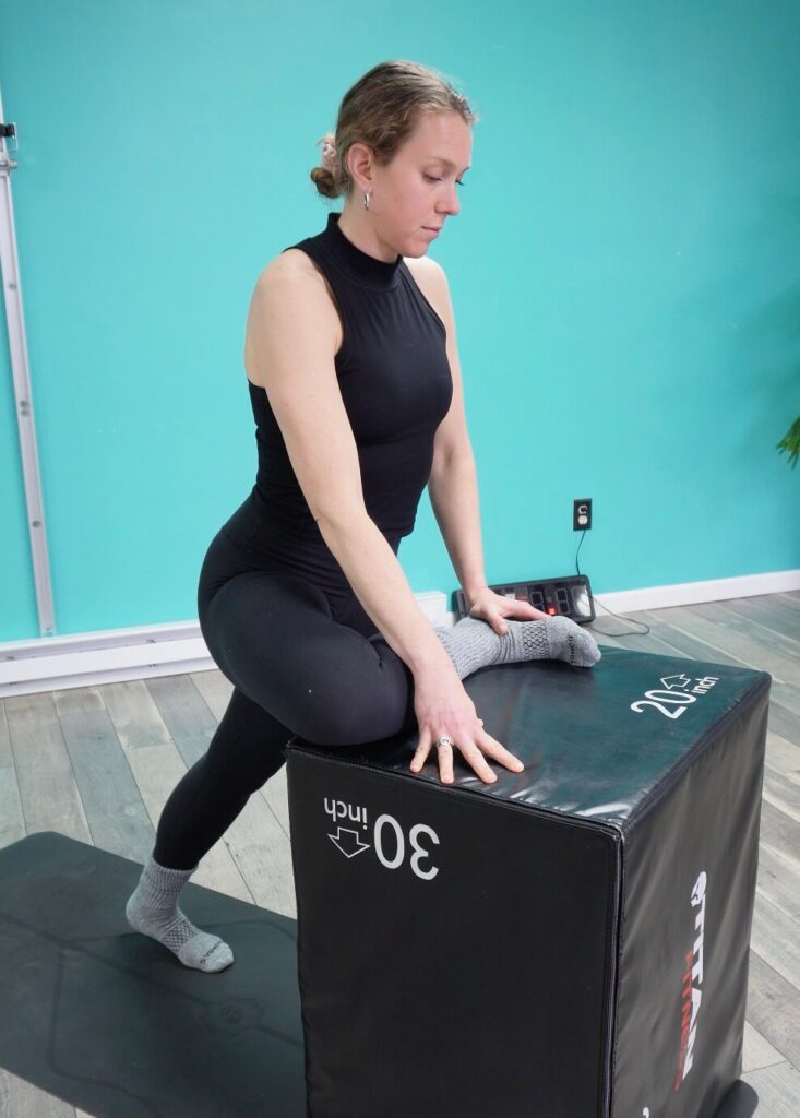 Dr. Chloe with 1 leg elevated on a box with her shin parallel to her hips stretching her hip and glutes